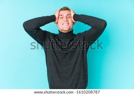 Young caucasian man on a blue background laughs joyfully keeping hands on head. Happiness concept.
