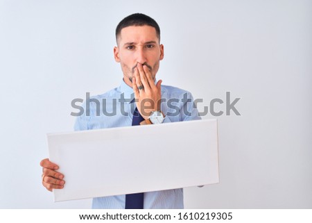 Young business man holding blank banner over isolated background cover mouth with hand shocked with shame for mistake, expression of fear, scared in silence, secret concept