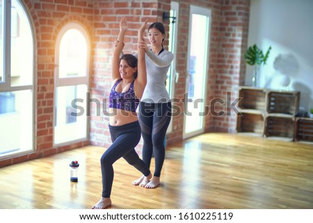 2 young beautiful sportswomen practicing yoga. One of them teaching warrior pose at gym