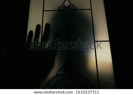 A silhouette man standing behind the door,hand on the window, Thriller concept, Blurred edit