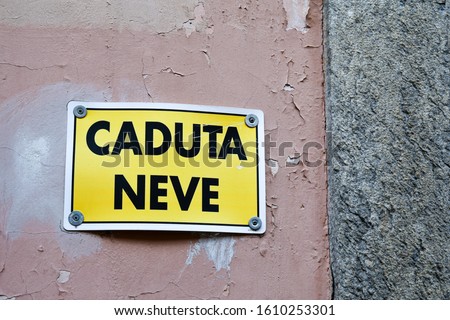 Close-up of an old wall with a warning sign that says: "Snow fall" (Italian: Caduta neve), warning of the danger of falling snow from the roofs of houses, Dronero, Cuneo, Piedmont, Italy