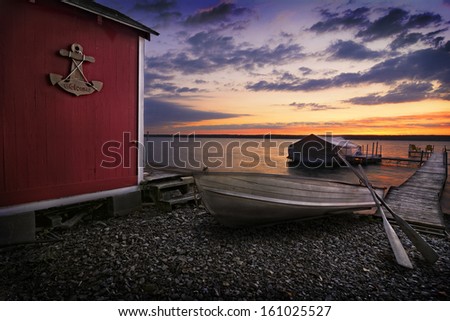 A beautiful place to watch a sunrise on Lake Cayuga in the Finger lakes region of New York state. To the left is a red storage shed with a wood anchor sign that says Welcome on it. 