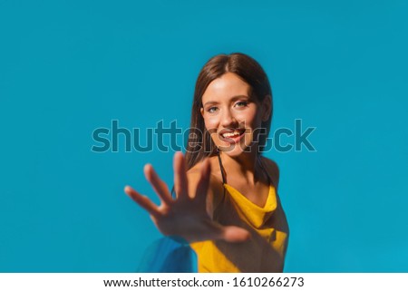Beautiful female on a blue background with long dark hair and in an orange beach dress snatches a proposal. Emotional joyful girl of Caucasian appearance with a smile