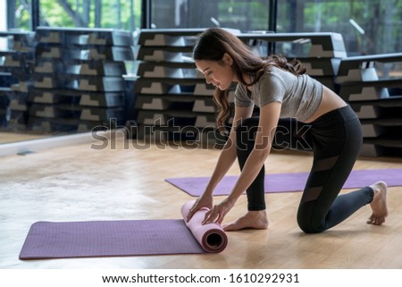Asian woman rolls her mat after studying yoga at fitness club. Royalty-Free Stock Photo #1610292931