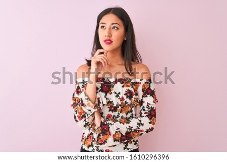Young chinese woman wearing floral t-shirt standing over isolated pink background with hand on chin thinking about question, pensive expression. Smiling with thoughtful face. Doubt concept.