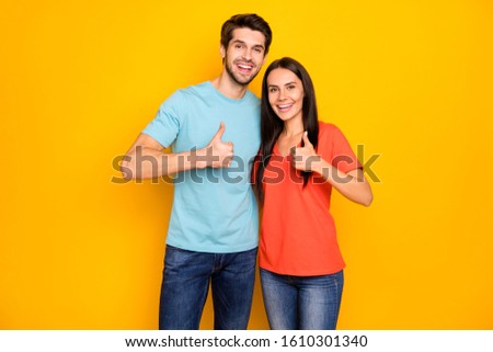 Photo of funny two people couple in love guy lady hugging raising thumb fingers expressing agreement wear casual blue orange t-shirts jeans isolated over yellow color background