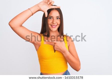 Young beautiful girl wearing yellow casual t-shirt standing over isolated white background smiling making frame with hands and fingers with happy face. Creativity and photography concept.