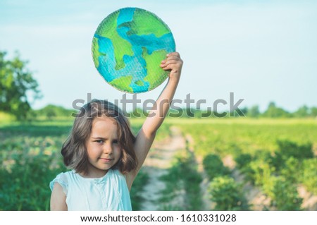 Protection and love of earth. Little girl holding planet in hands against green spring background. Earth day holiday concept. Environmental Conservation