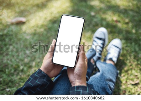 Mockup image of a woman holding black mobile phone with blank white screen while sitting in the outdoors
