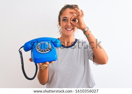 Young redhead woman holding classic retro telephone over isolated background with happy face smiling doing ok sign with hand on eye looking through fingers