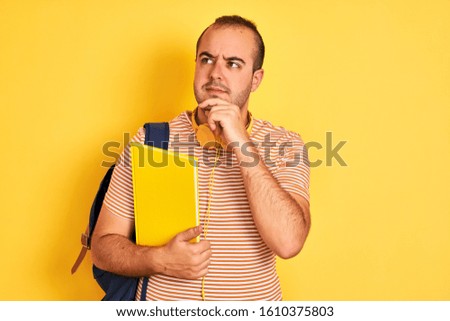 Student man wearing backpack headphones holding notebook over isolated yellow background serious face thinking about question, very confused idea