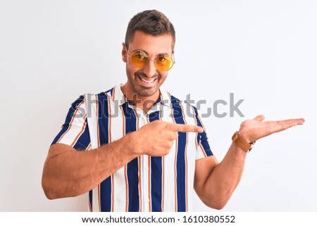 Young handsome man wearing summer sunglasses over isolated background amazed and smiling to the camera while presenting with hand and pointing with finger.