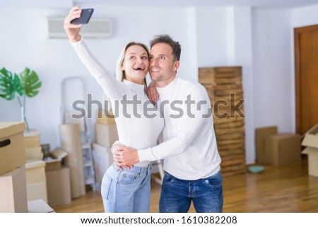 Young beautiful couple standing using smartphone to take selfie at new home around cardboard boxes