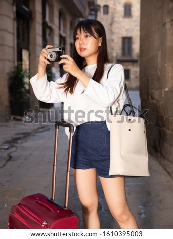 Smiling young girl holding camera in hands and photographing in city