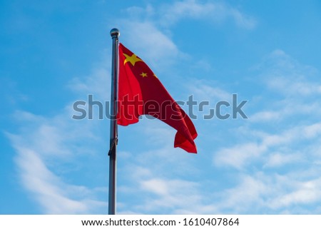 Chinese red flag on a flagpole against a blue sky with clouds.