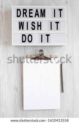 'Dream it, wish it, do it' words on a modern board, clipboard with blank sheet of paper on a white wooden background, top view. Overhead, from above, flat lay. Copy space.
