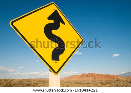 Black curving arrow on bright yellow roadsign pointing ahead to stark desert landscape