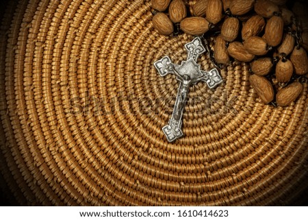 Close-up of an old silver crucifix with Jesus Christ and wooden rosary bead on brown woven wicker texture