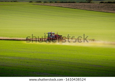 An agricultural tractor with outspread spraying arms  spreads green chemicals on a field in Hertfordshire, UK Royalty-Free Stock Photo #1610438524