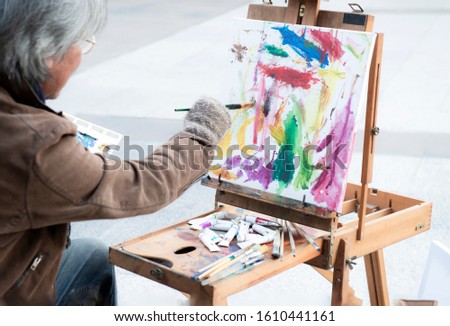 Street artists man sitting and painting abstract colourful on canvas at the street of Bangkok.Lifestyle of painter (artist) painting an abstract cheerful celebrated on canvas.Holiday and hobbies.