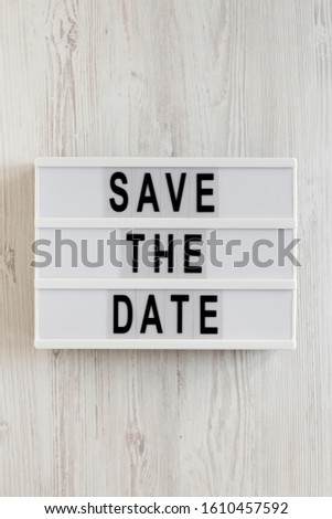 'Save the date' words on a lightbox on a white wooden surface, top view. Overhead, from above, flat lay. Close-up.