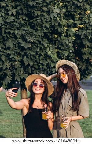 Two pretty girls take selfie in the summer outdoors at sunset. Girlfriends have fun, laugh, smile and take pictures. Closeup portrait of two young women in straw hats.