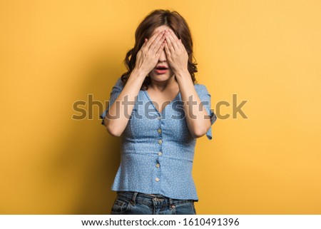 shocked girl covering eyes with hands on yellow background