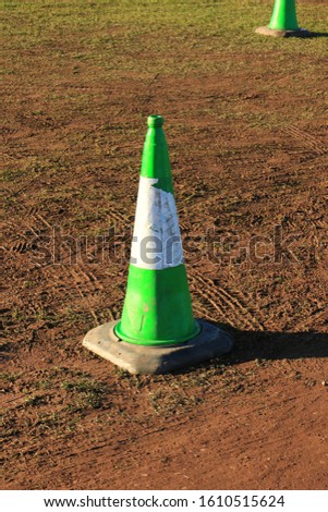 Full length of a green traffic cone on a muddy car-park