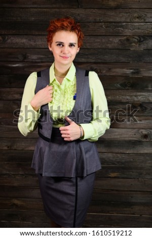 Art portrait of a pretty business woman with short red hair in a gray business suit on a wooden background. Standing right in front of the camera in various poses.