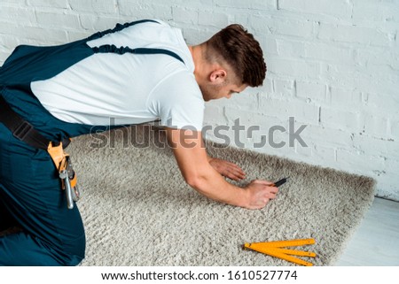 installer in overalls holding cutter near carpet Royalty-Free Stock Photo #1610527774