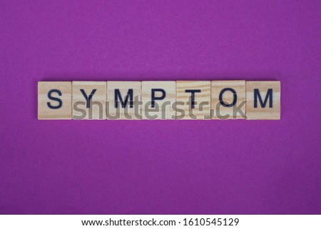 word symptom from small gray wooden letters lies on a lilac background