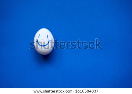 One white egg with a painted funny smiley on a blue background.