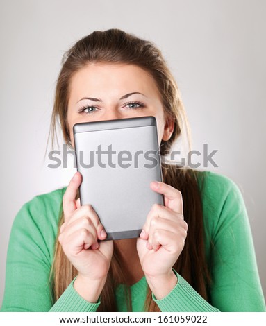 Young woman sitting on the desk and holding computer plane-table , isolated on grey background