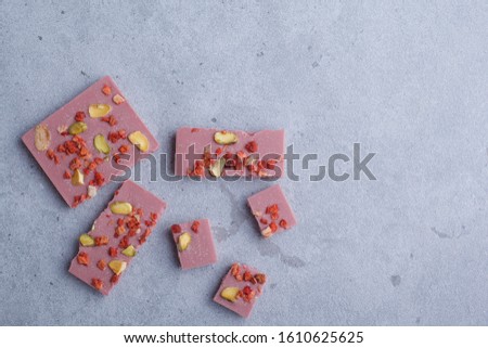 Pink chocolate with pistachios and strawberries on a grey background.