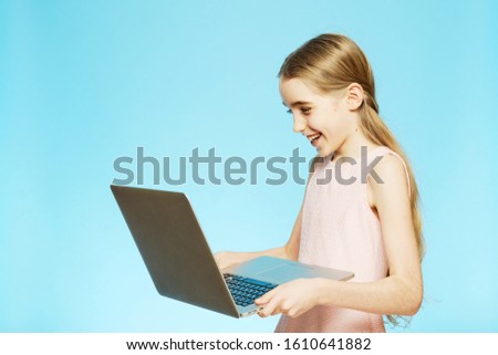 Isolated girl is having fun looking at the computer on a blue background. The concept of emotions. Distance learning online education