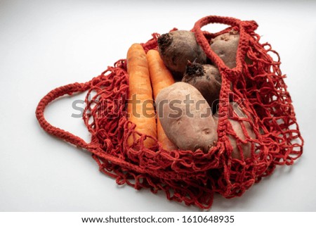 Trendy net shopping bag with potatoes on gray background. Ugly, unnormal vegetable, zero waste and plastic free concept. Copy space.