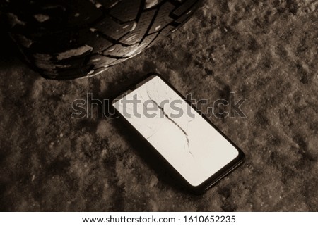 the smartphone screen is cracked from moving a car tire over it at night, the front and back background is blurred with a bokeh effect