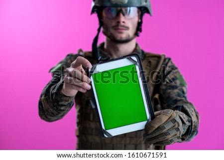 army soldier showing a tablet computer with a blank green screen isolated on pink background