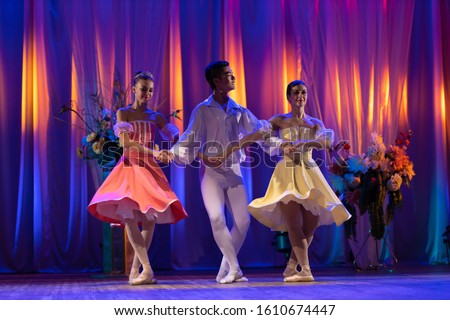 Trio of young girls ballerinas and a young man dancing ballet performance on stage in the theater on a blue purple background