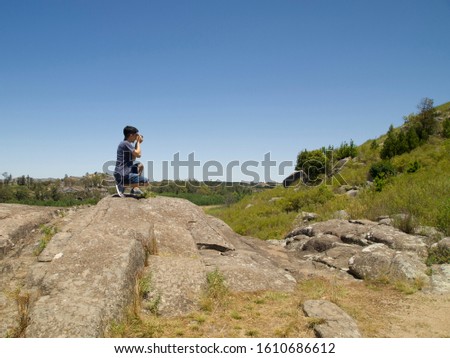 Young argentinian photographer taking a picture at the top of a rock. Photography, shooting concept.