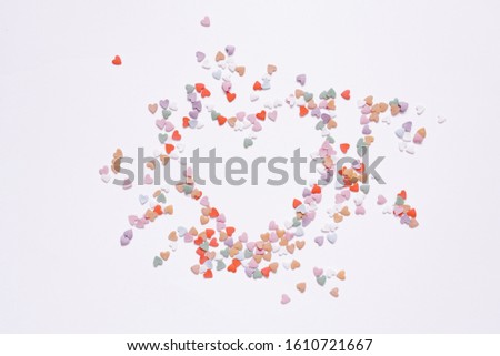 Confetti of small multicolored hearts on a white background with an empty space in the form of a heart. Creative background for Valentine's day greeting card with copy space