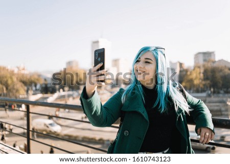 Smiling girl with blue hair and eyeliner taking selfie