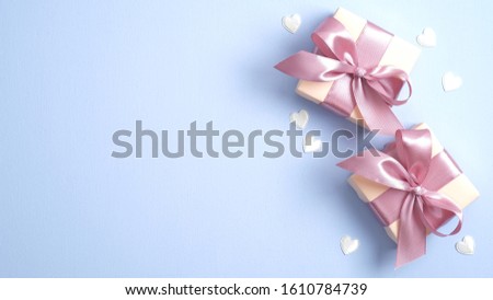 Valentine gift boxes with pink ribbon bow on pastel blue background with heart shaped confetti. Valentines or Mother day banner design. Flat lay, top view, copy space. 