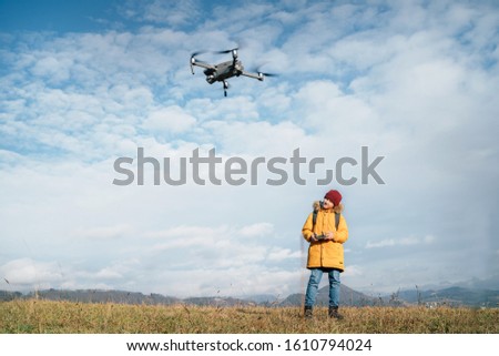 Teenager boy dressed yellow jacket piloting a modern digital drone using remote controller