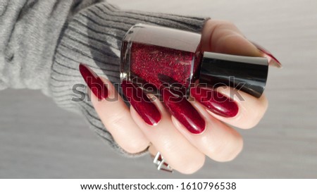 Female hand with long nails and red manicure with bottles of nail polish