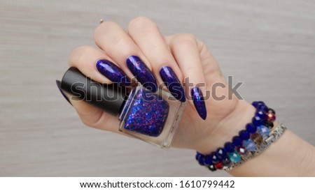 Female hand with long nails and a bottle of purple lilac color nail polish