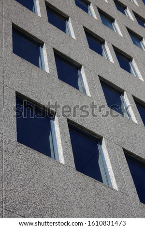 Windows. Contrast low-angle photo of multistory building. Modern architecture image with perspective. Urban real estate. Diagonal composition of concrete facade wall with reflection of bright blue sky