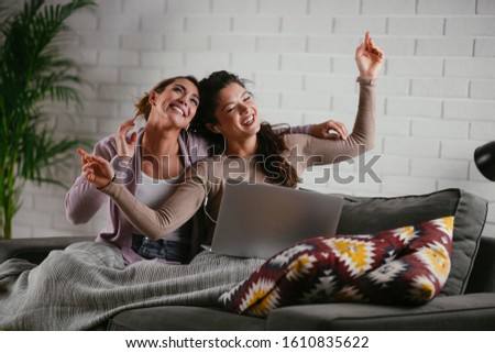 Girlfriends dancing and listen music from a laptop computer at home. Girls having fun at apartment.