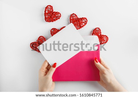 Pink envelope in hands and red hearts on a white background for Valentine's Day. Blank sheet - concept for design. 