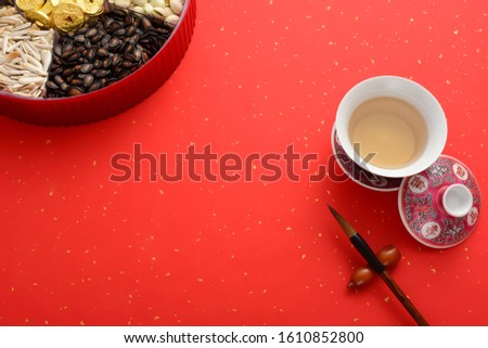 Tea cup, snack fruit plate and brush on red background, traditional Chinese New Year.Translation of text appear in image: Blessing and treasure.